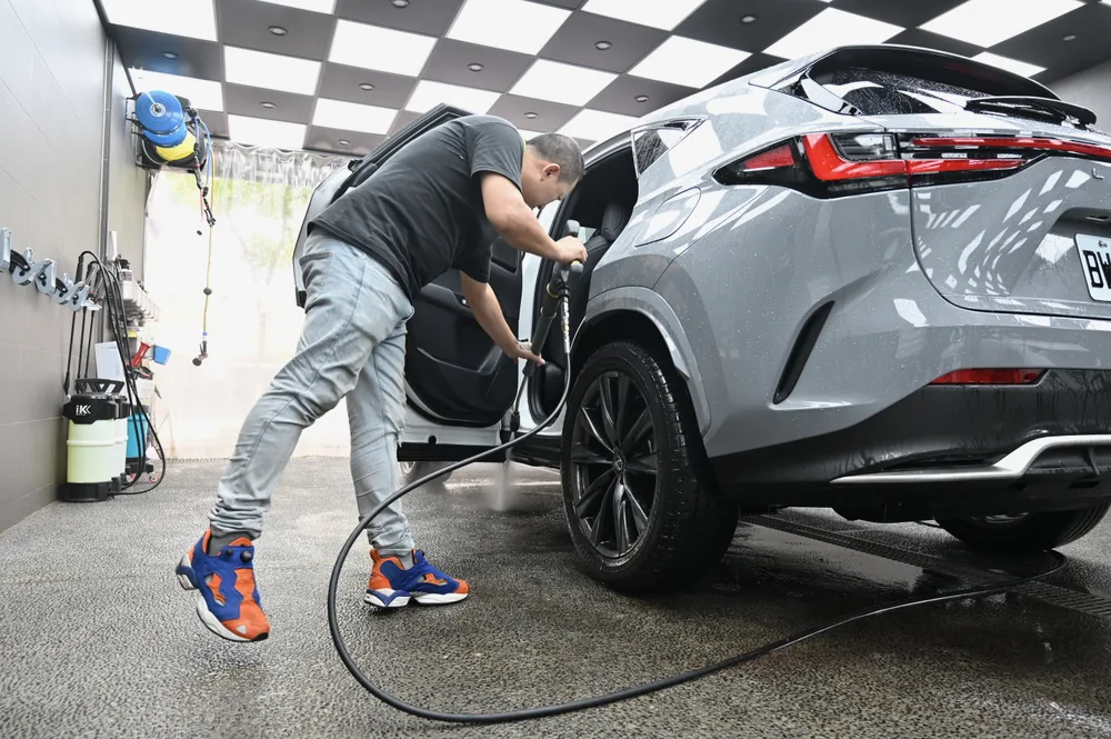 技師以高壓水槍沖洗 Lexus NX 車尾與後保桿,帶走膜面附著的塵砂