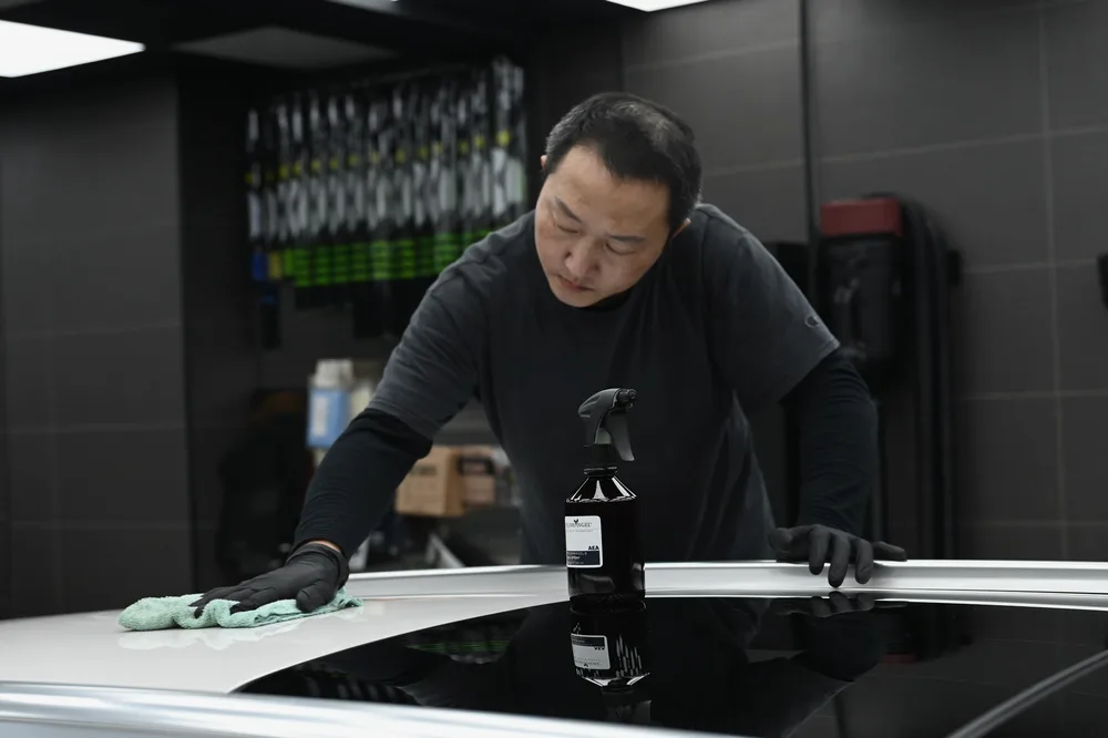 技師伸長手臂擦拭車頂，帶行李架的旅行車頂面逐段收乾