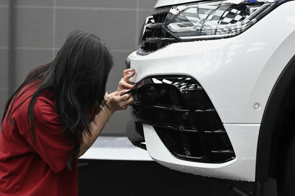 施工人員以手指沿白色 Volkswagen Tiguan 前保桿下方進氣壩邊緣壓合保護膜