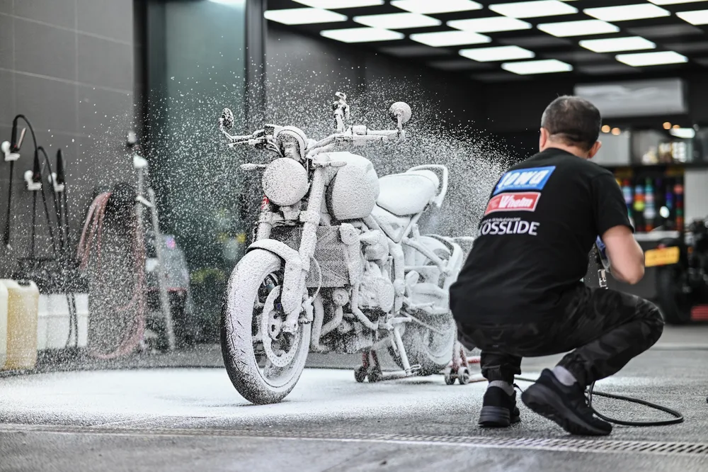 技師以雪泡覆蓋整台 Triumph 重機車身與輪圈，進行鍍膜前的洗車除塵